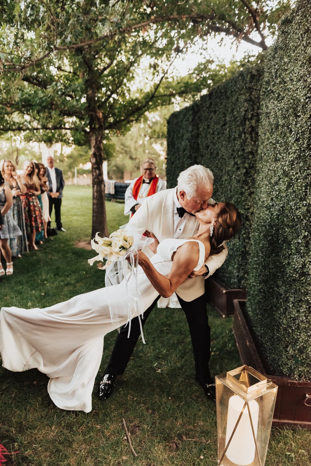 Real outdoor wedding first-kiss moment among greenery at golden hour