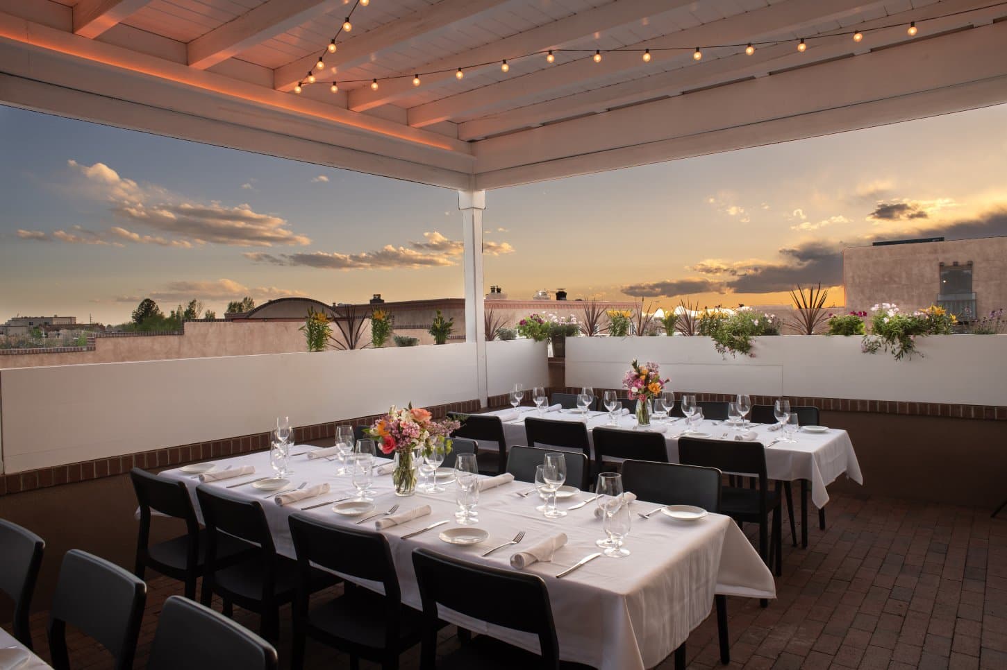 A reception table set for dinner on The Sunset Terrace balcony overlooking downtown Santa Fe rooftops at sunset
